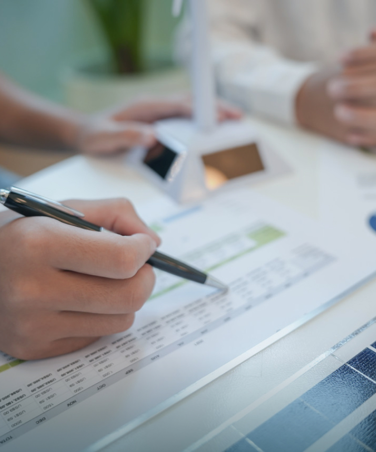 Close-up of a person analyzing solavita solar project data with a pen and financial report on the desk.