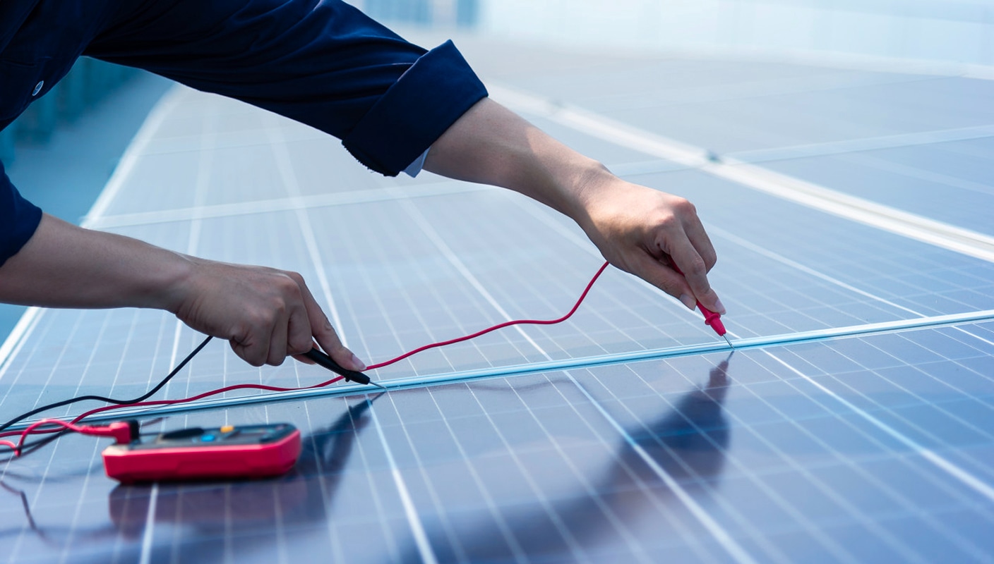 A technician is testing the performance of a solar panel using a multimeter, checking the electrical connections with red and black probes. The image highlights the meticulous inspection of the solar cells for proper functionality.