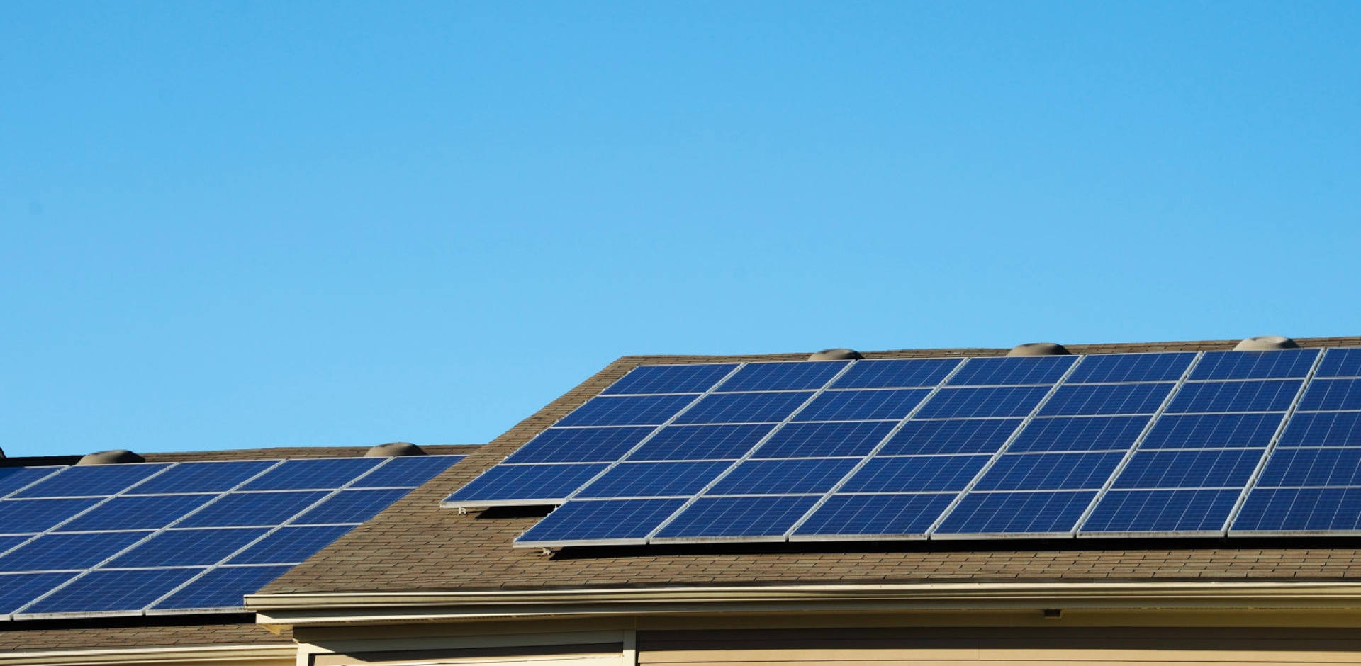 Rooftop solar panels on a modern suburban home under clear blue sky.
