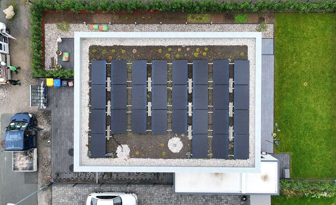 Top-down view of a modern residential building with a flat rooftop solar system installed in neat rows, surrounded by landscaping and a well-maintained urban neighborhood