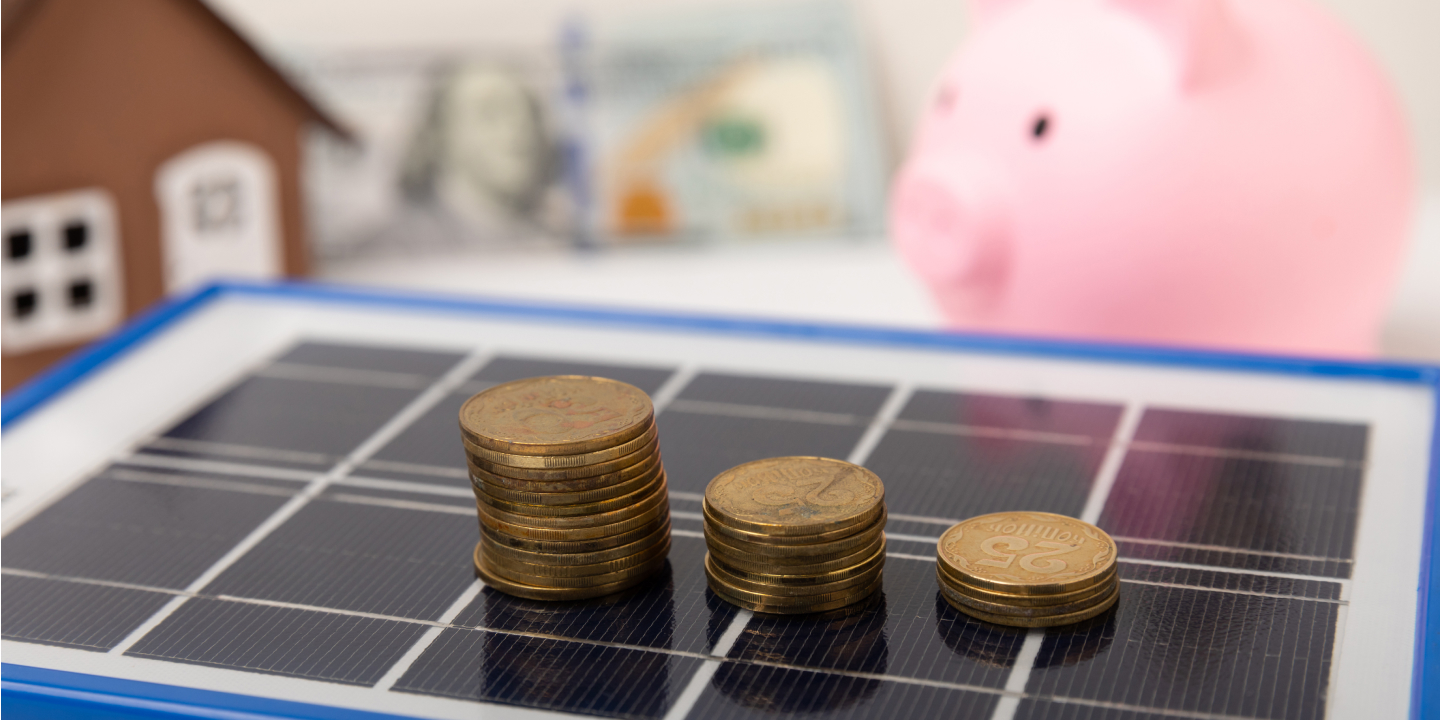 Stacks of coins on solar panel with piggy bank and house model in background