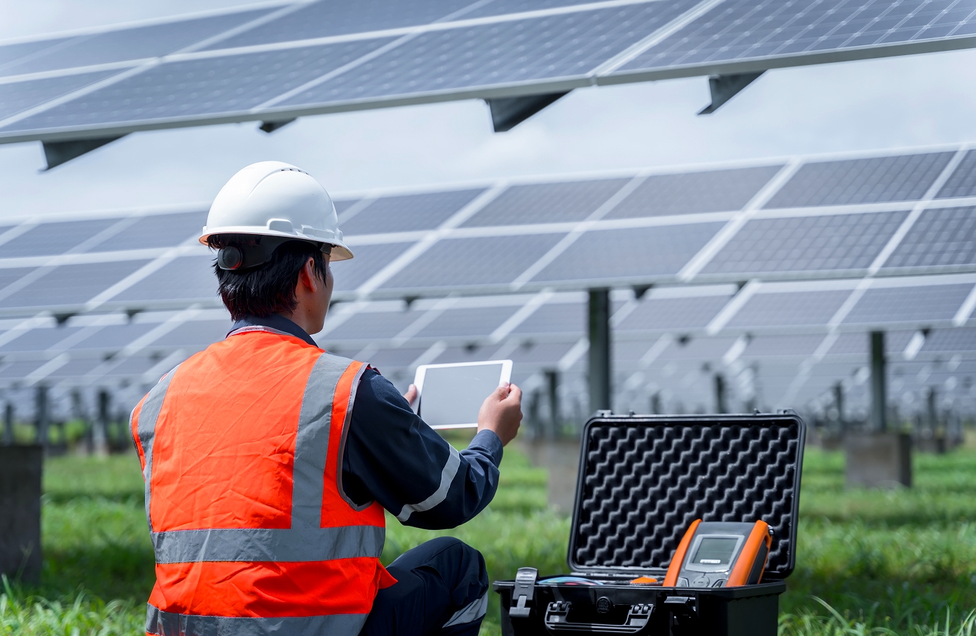 Solavita technician with a tablet inspecting a solar power plant, standing near rows of photovoltaic panels, with testing equipment visible in an open case.