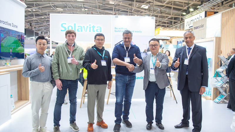 Solavita representatives and international partners celebrate a successful collaboration with a handshake and thumbs-up at a global renewable energy exhibition booth